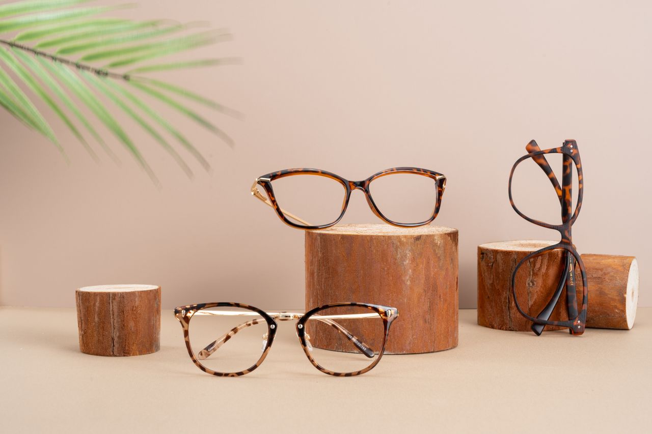 services-01 Chic glasses on wooden stands with a fern leaf backdrop, showcasing modern eyewear.