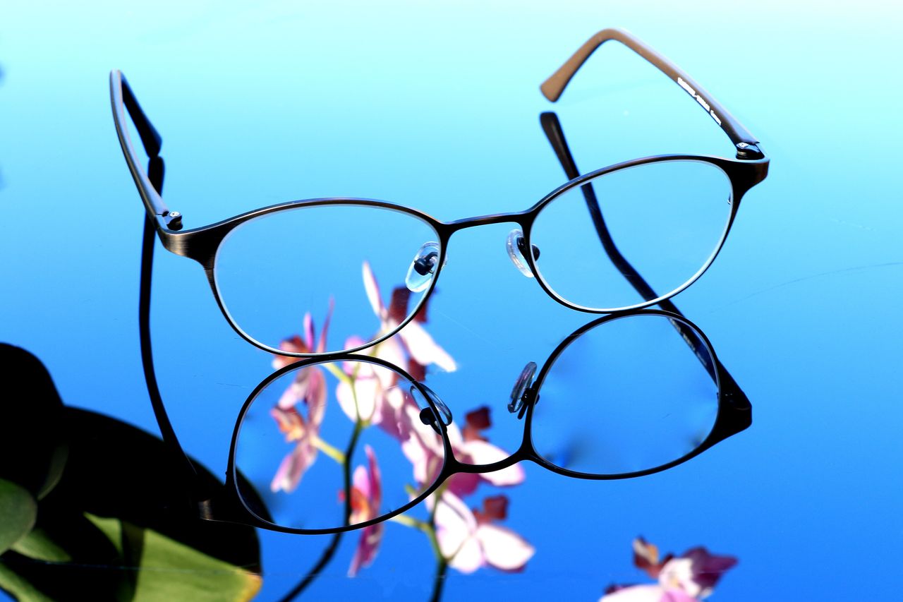 Stylish eyeglasses on reflective surface with orchid blossoms. Perfect for design inspiration.