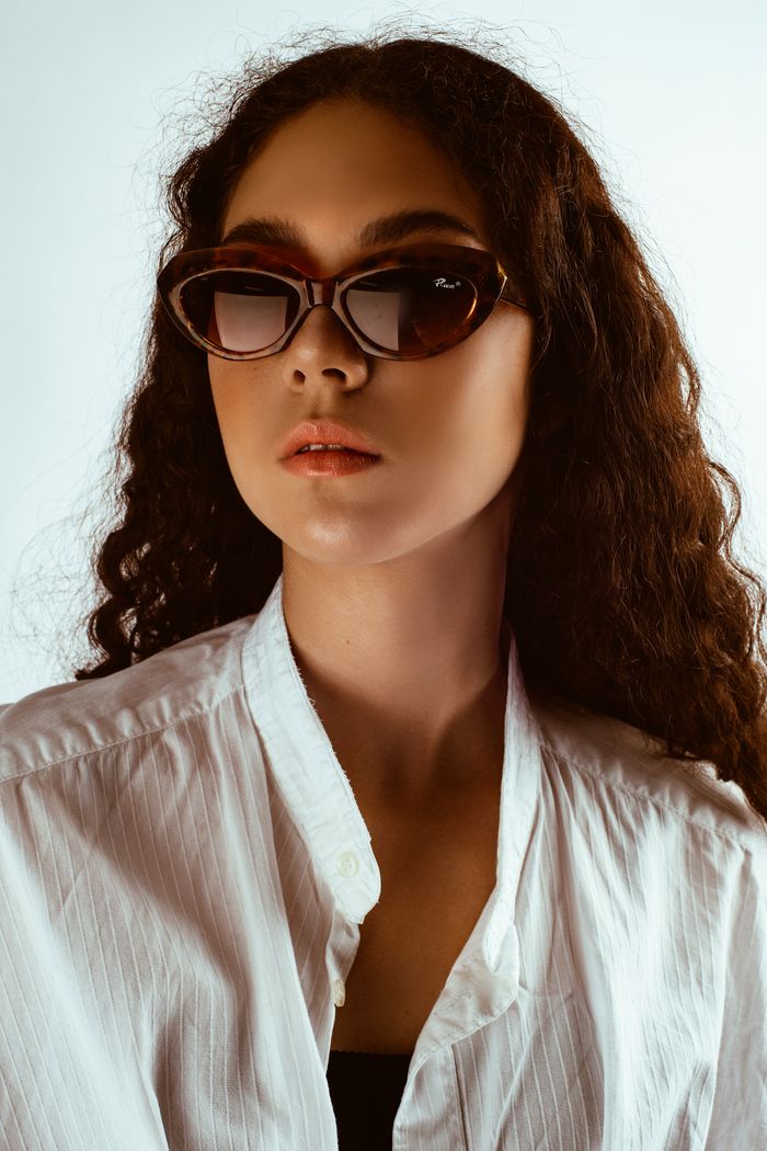Mastering the First Impression: Your intriguing post title goes here Portrait of a woman with curly hair wearing sunglasses and a white shirt.