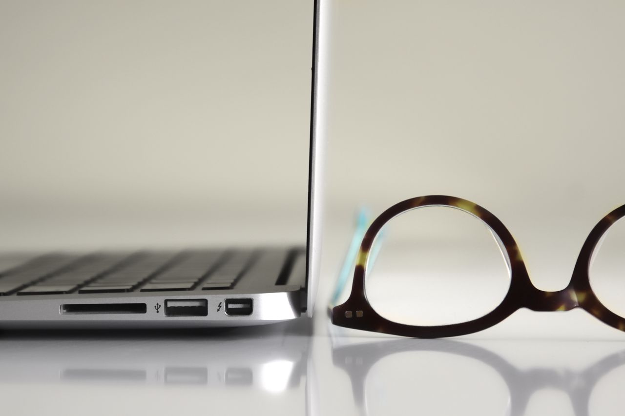 services-01 Side view of a modern laptop alongside stylish tortoiseshell glasses on a reflective surface.