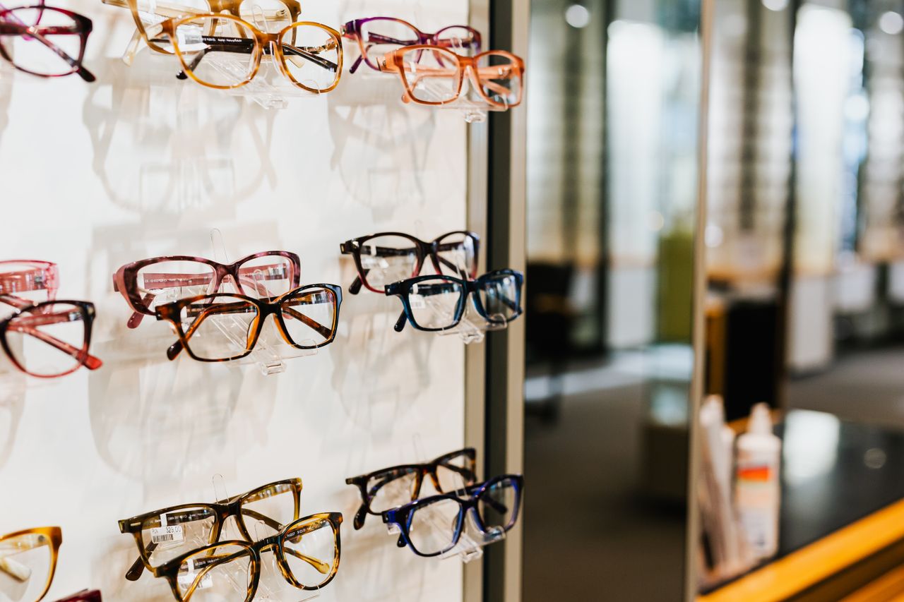 Assorted eyeglasses on a well-lit shelf in an optician's store.