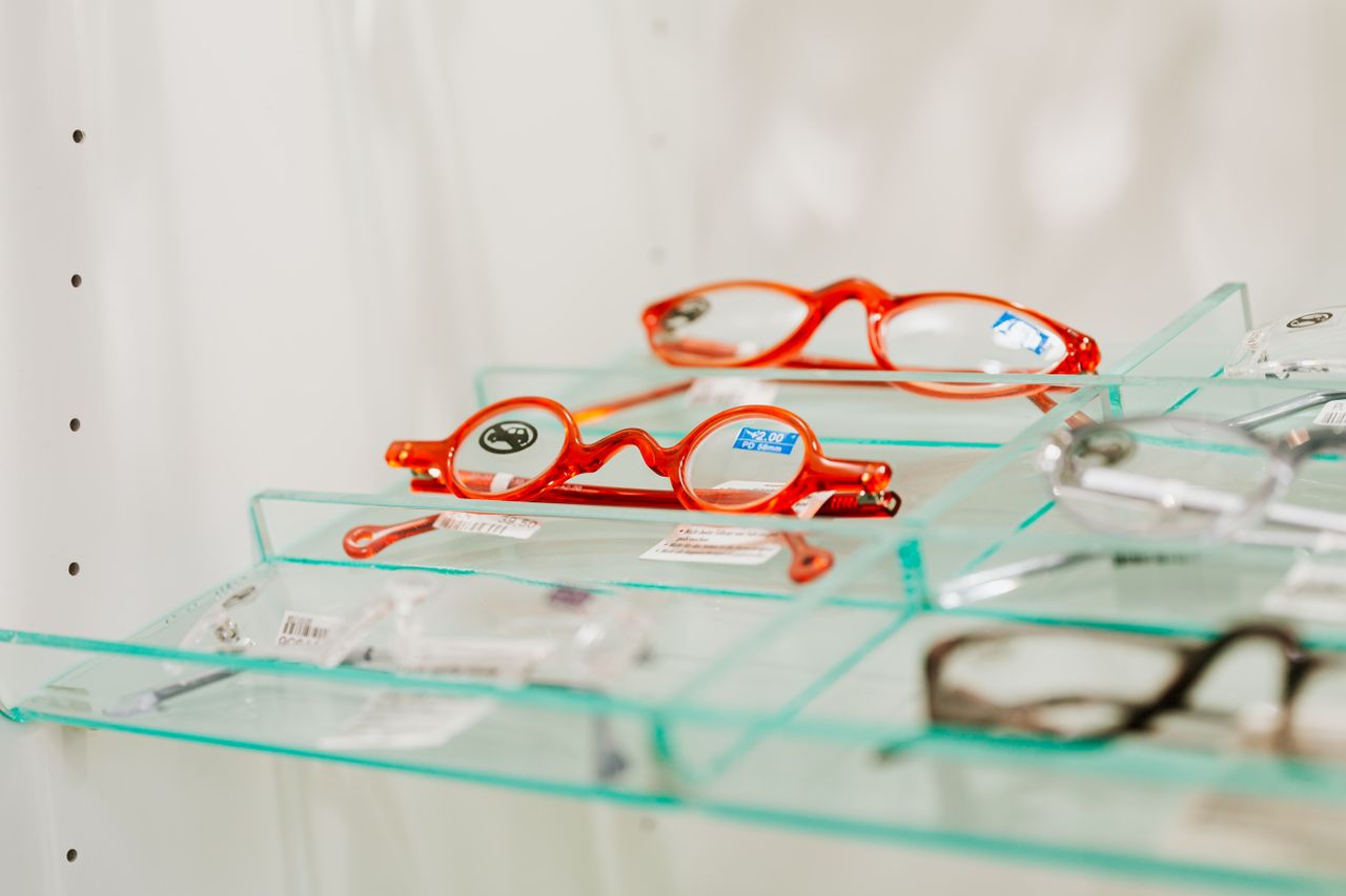 Stylish red eyeglasses displayed on a glass shelf in an eyewear store.