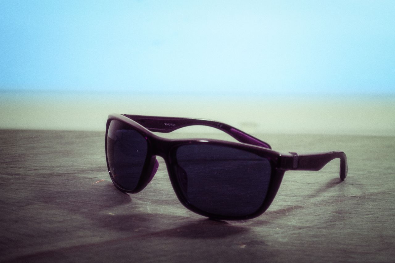 services-01 Black sunglasses with dark lenses on a wooden table by the beach offering chic summer protection.